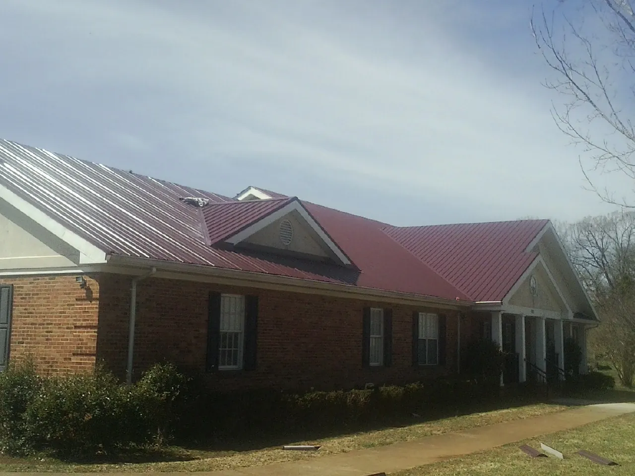 Red metal roof with gabled entries on a long brick building, from a Hail Damage Roof Repair job in Wyocena