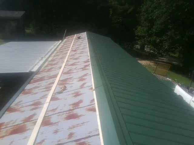 Old rusted panels beside newly installed green metal roofing — Wind Damage Roof Repair by Roofing Brothers in Wyocena