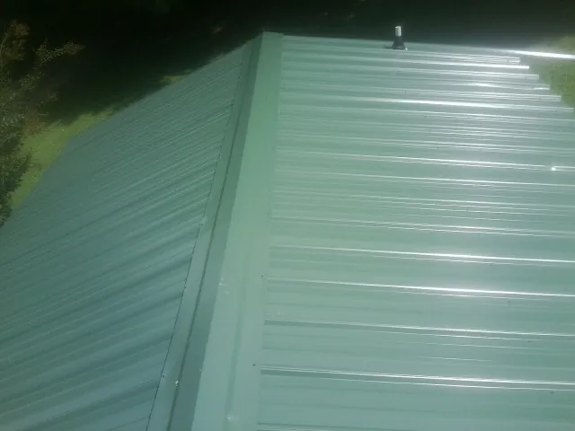 New green metal panels meeting at the ridge of a roof — Flat Roof Repair work by our crew in Wyocena