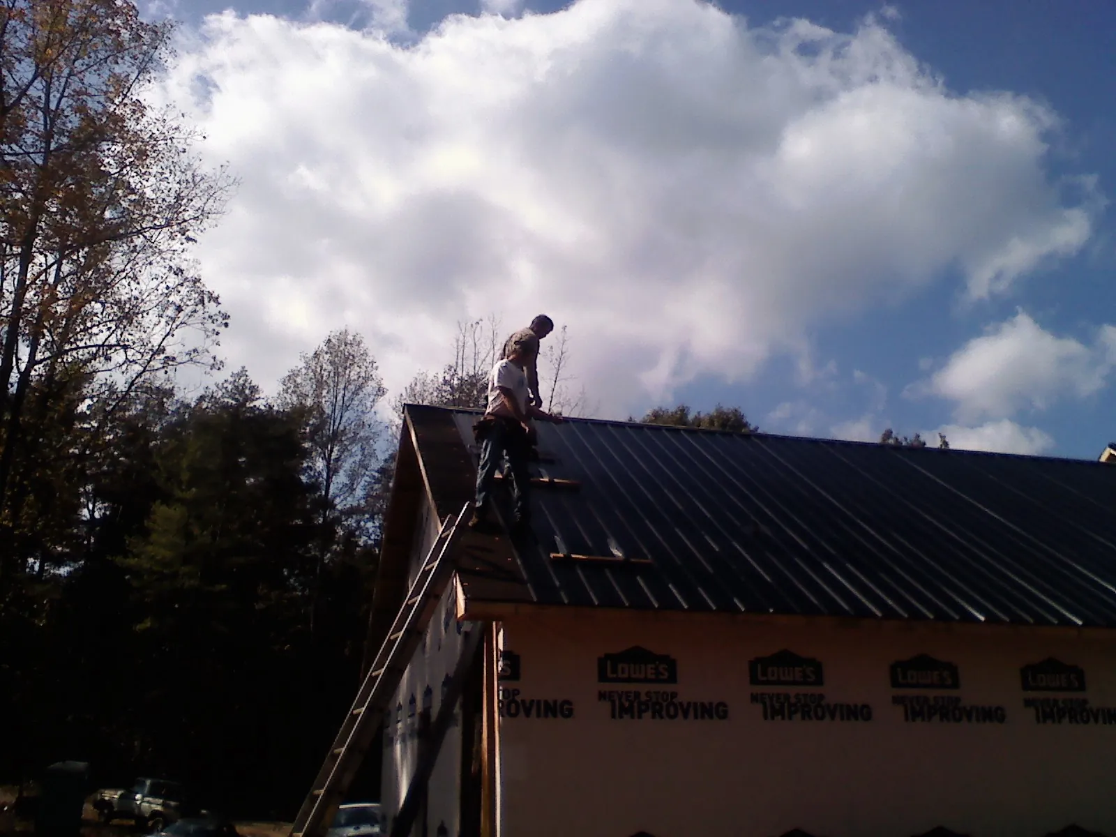 Roofer fastening dark metal panels high against a cloudy sky, from a Roof Inspection job in Wyocena