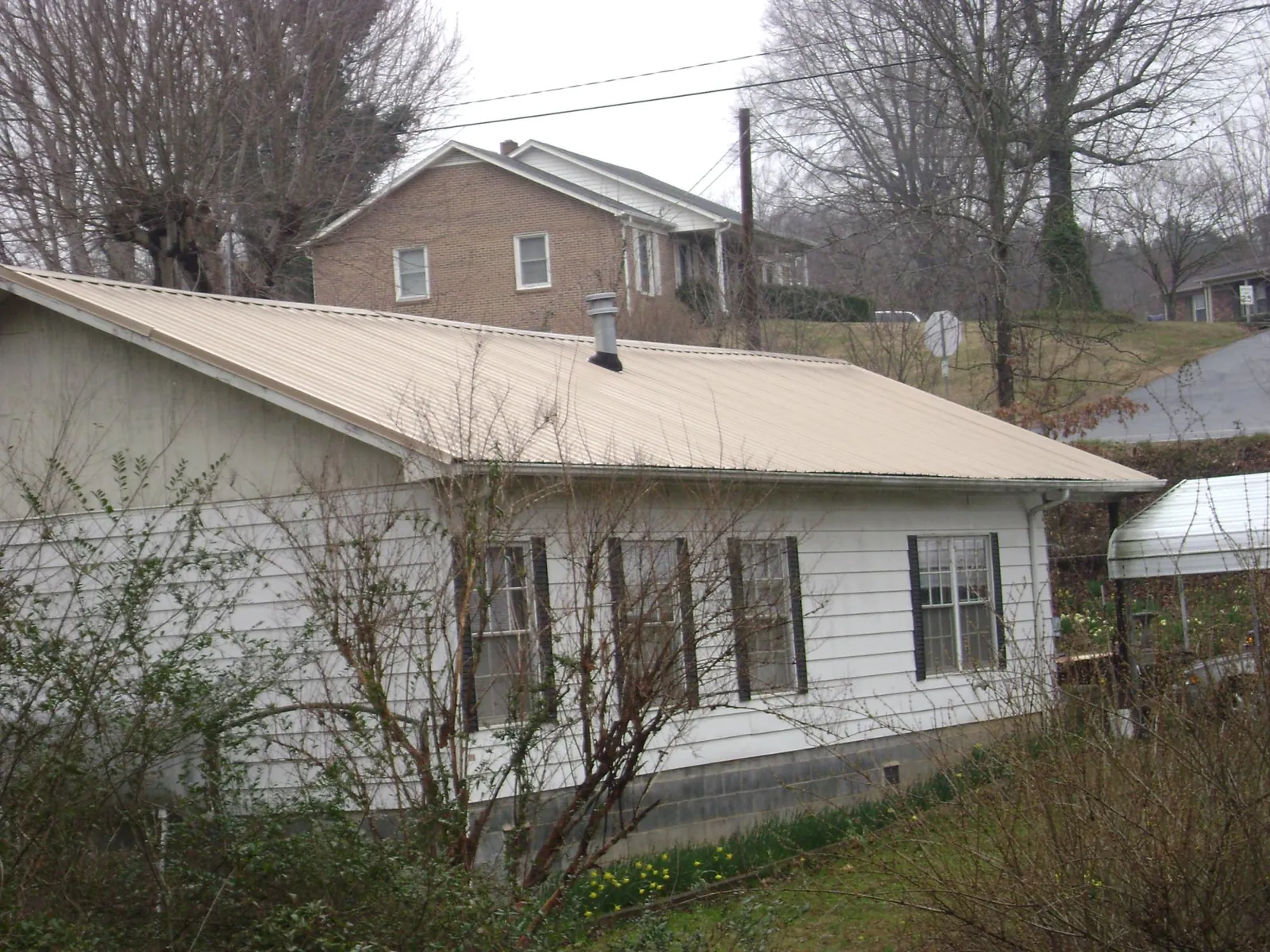 Tan metal roof on a white sided house set into a hillside — Commercial Roofing by Roofing Brothers in Wyocena